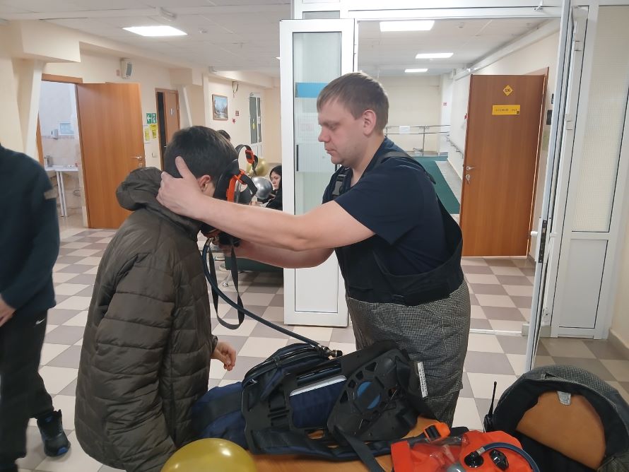 Пожарный помогает ребенку включиться в дыхательный аппарат