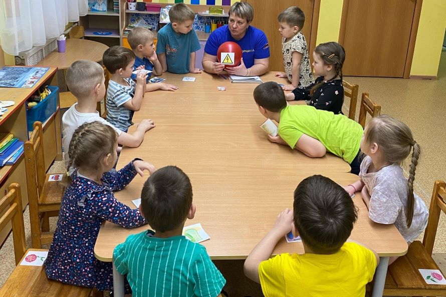 Дети, сидя за столом, внимательно слушают инженера пожарной охраны
