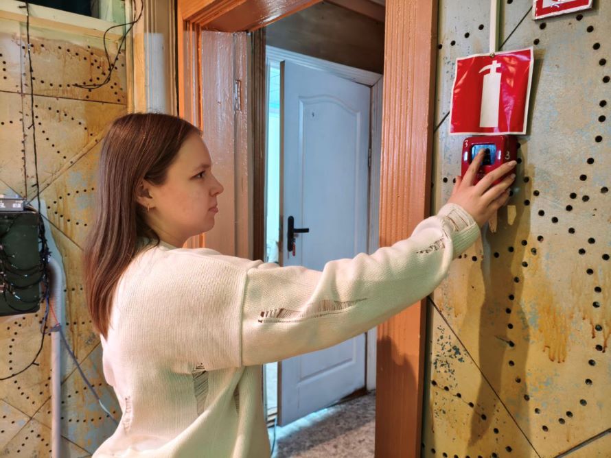 Сотрудник учреждения нажимает на кнопку ручного пожарного извещателя