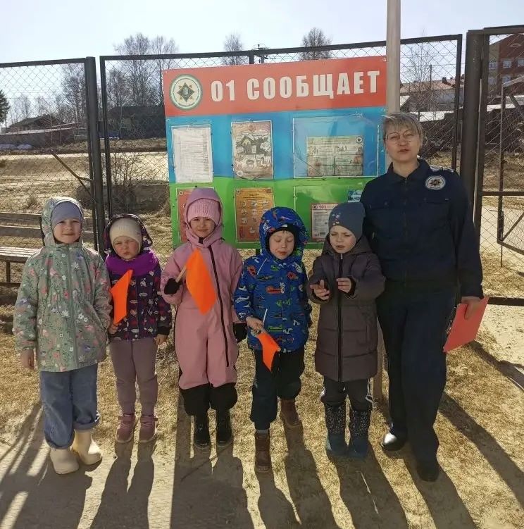 Фото детей и инструктора пожарной охраны на фоне доски для памяток