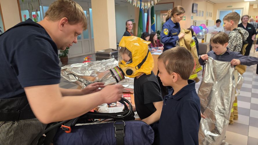 Пожарный помогает мальчику примерить экипировку